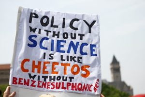 A protester at the People's Climate March near the Trump Hotel holding a sign saying "Policy without science is like cheetos without benzenesulfonic acid."