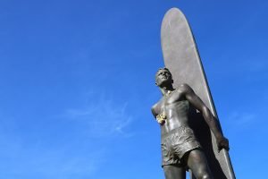A bronze statue in Santa Cruz, California of a surfer with a lei of flowers around his neck.