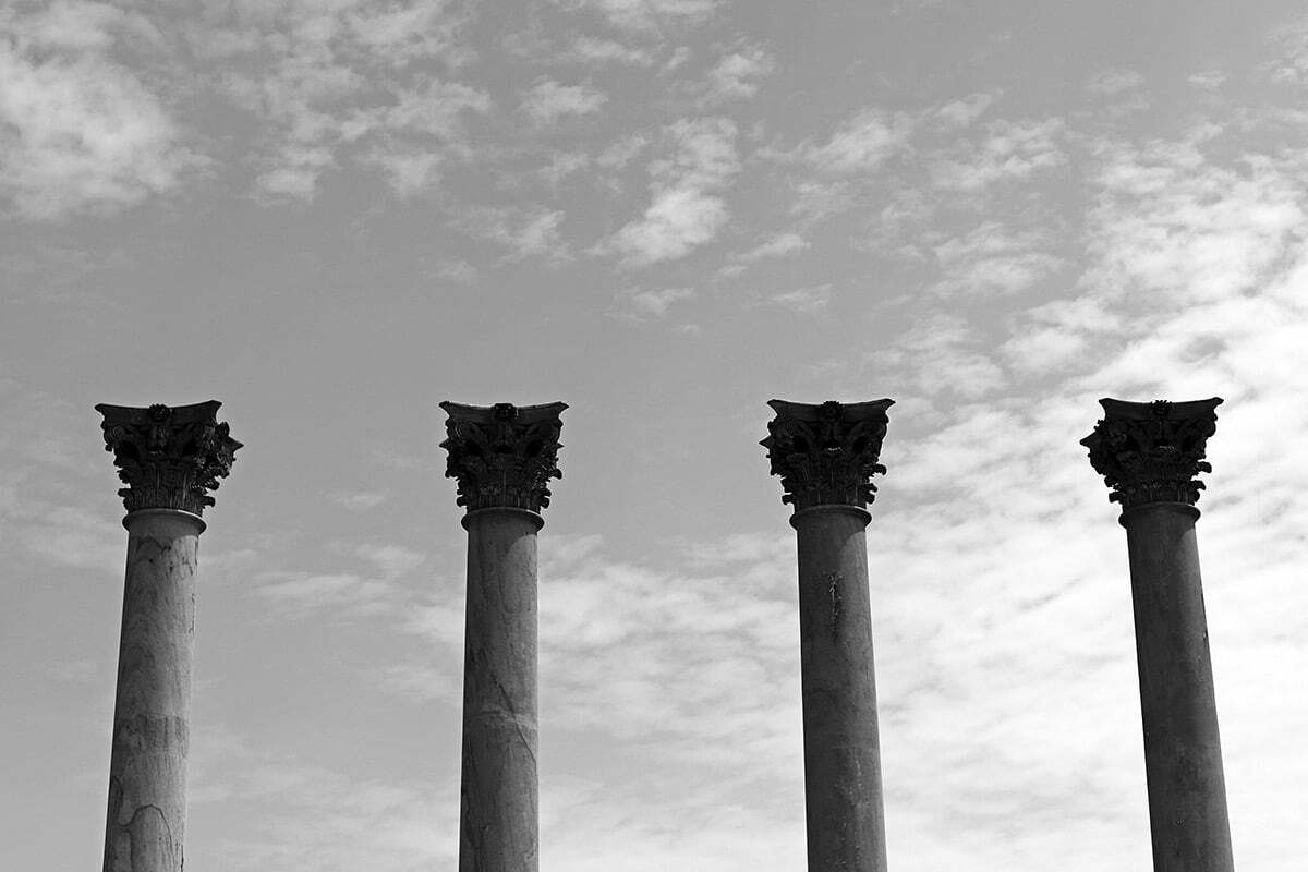 A black and white photograph of four classical columns and a cloudy sky seen at the National Arboretum.