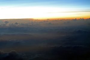 An orange sunset breaks over the clouds as seen from a plane over the Caribbean Sea.