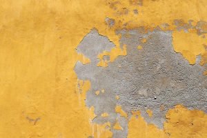 A concrete wall with bright yellow paint peels and cracks in Cartegena, Colombia.